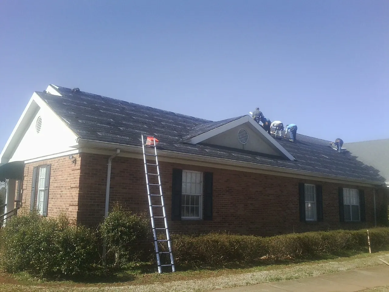Crew tearing shingles off a brick ranch roof with a ladder set — Metal Roof Repair work by our crew in Williamsport